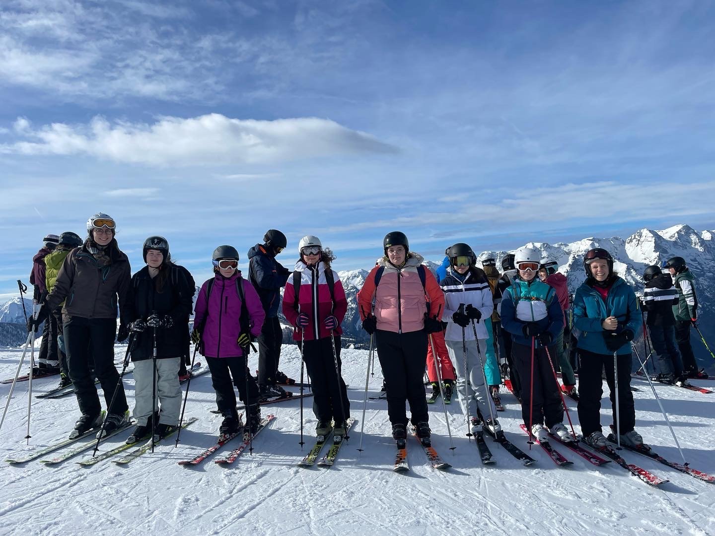 Acht Schifahrer*innen vorm Abfahren, im Hintergrund die Berge
