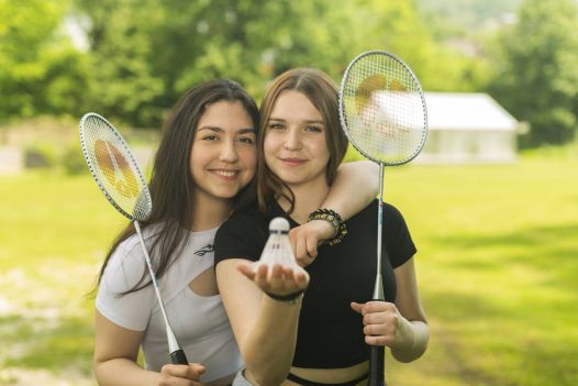 Zwei Schülerinnen sind umarmt und halten Badmintonball in die Kamera